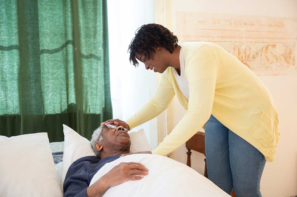 Elderly care worker helping an older man in bed