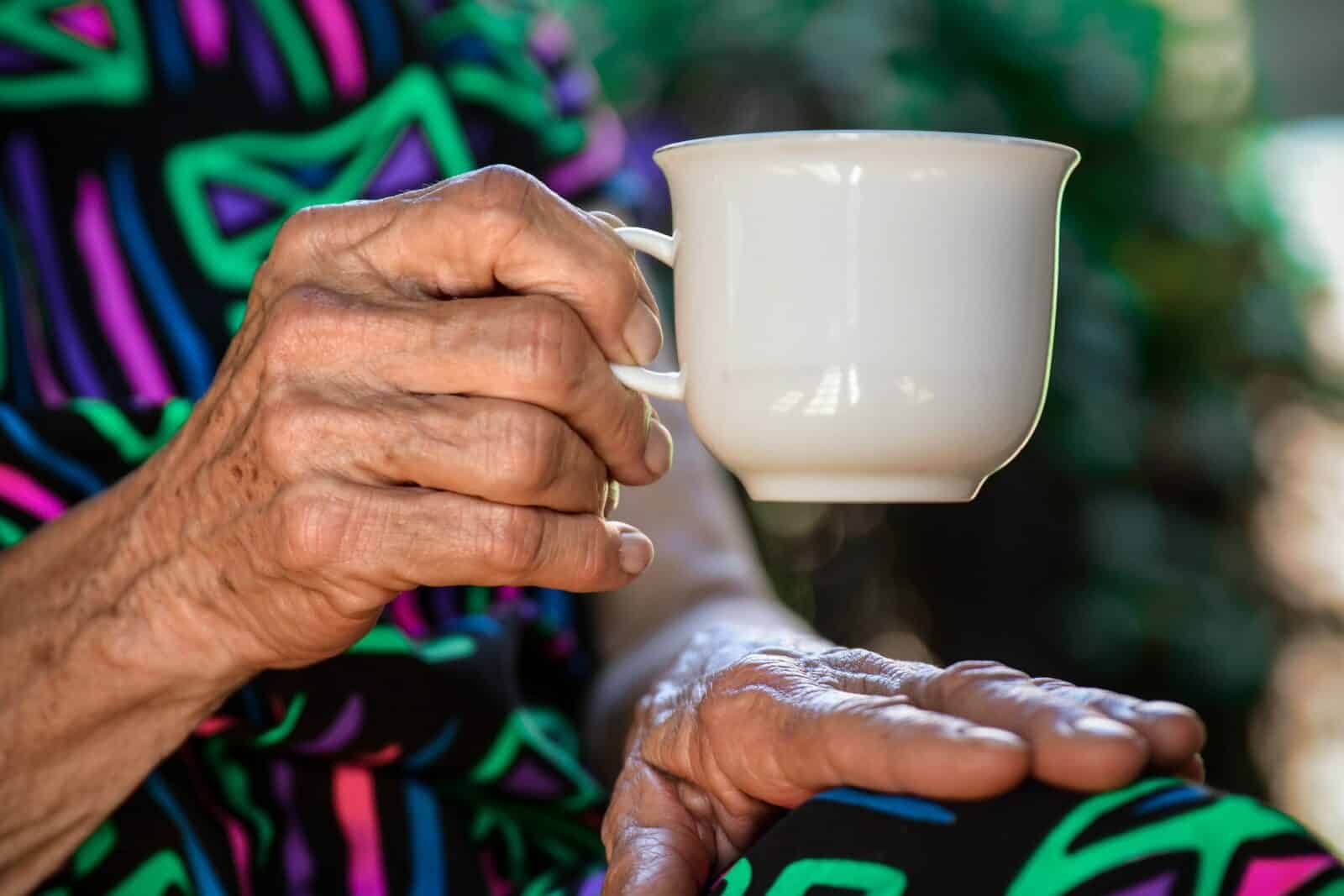 close up of elderly persons hand holding a small white tea cup