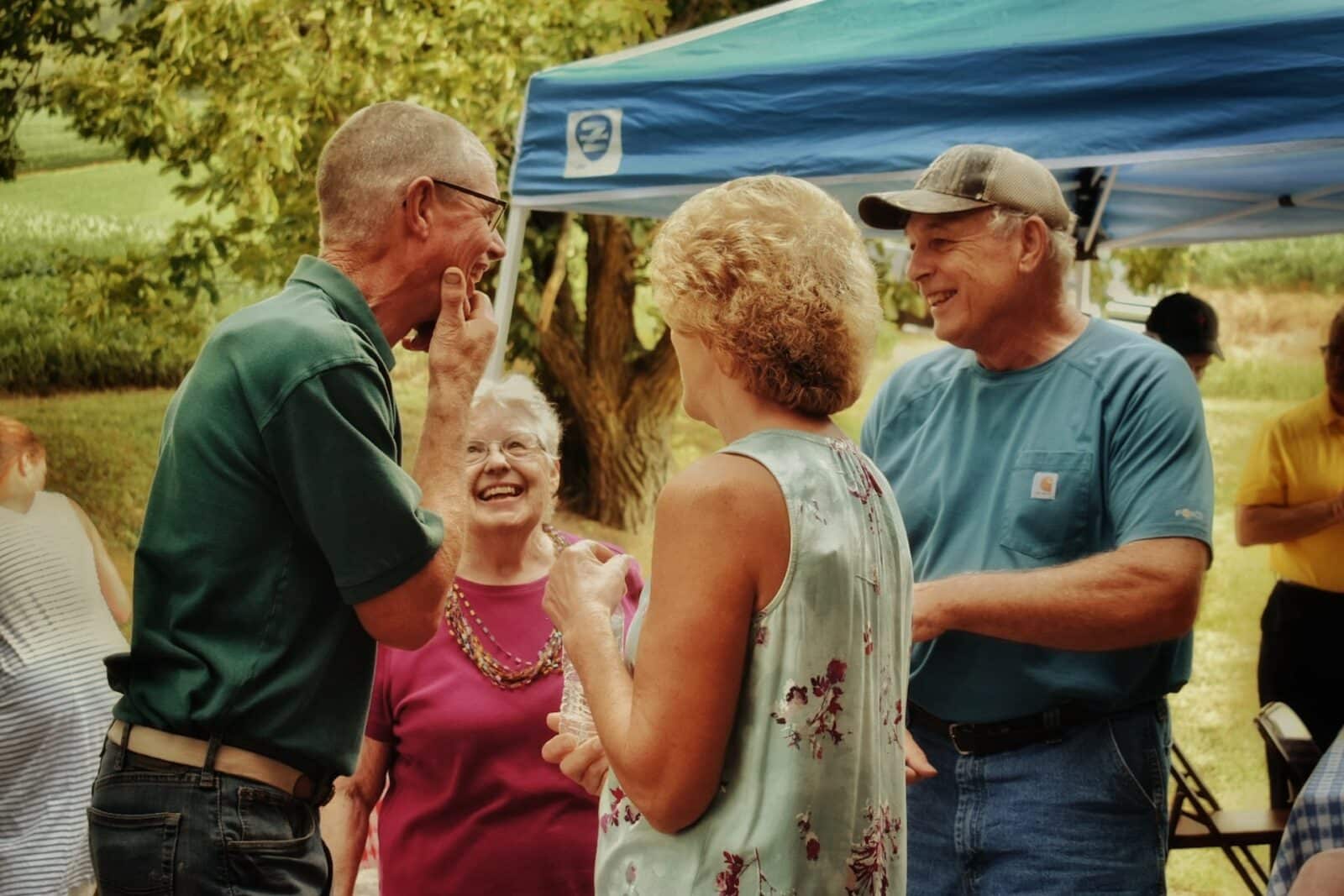group of people standing outdoors in front of a pop up canvas tent speaking